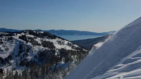A skier skiing deep powder on a ridge line at Alpine Meadows with Lake Tahoe in the background