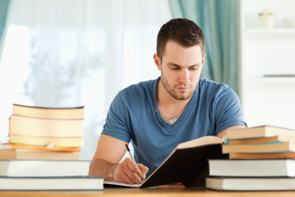 A man studying, surrounded by books. 